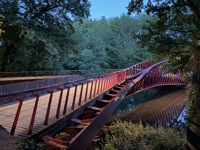 Modern lines meet medieval woods—the red footbridge crossing into another quiet corner of Bruges.